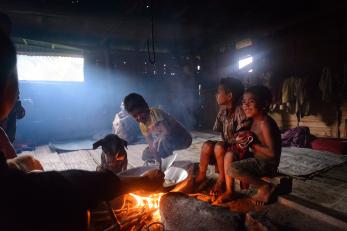 Children smile near a fire where food is cooking in a bowl in timor leste