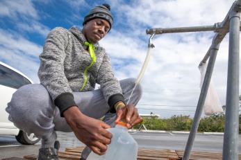 Bahamian man fills a water jug at a spigot.