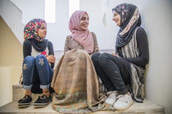 A mercy corps volunteer girls’ science teacher, talks with her students while they sit on stairs.