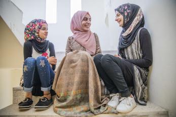 A mercy corps volunteer girls’ science teacher, talks with her students while they sit on stairs. 