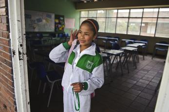 A young person stands in a doorway to a classroom.
