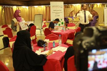 Two presenters address people sitting at tables during a seminar on coronavirus disease 2019.