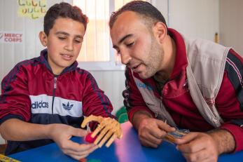 A young person works with mercy corps shadow teacher saleh alshalabi, learning how to strengthen his muscles and use his new prosthetic hand.