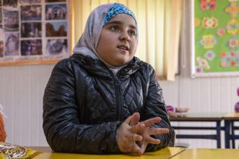 A young person sits at a table with their hands together.