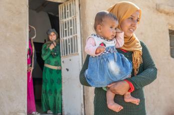 A person holds a child in front of their mother's home.