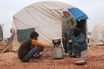 Two individuals sit in front of their tent in al-rayyan camp while speaking with an adult.