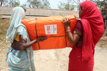 Two people carrying a shelter kit.