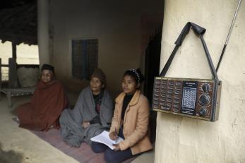 A student from the tharu community sits with elders as she listens to lessons on the radio in kailali district.