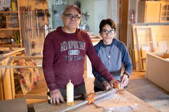 A carpenter and their son pose while working.
