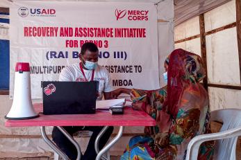 A mercy corps team member registering a community member for monthly e-vouchers so she can purchase food for her family.