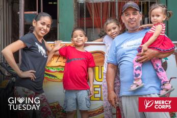 A mercy corps’ venesperanza program participant standing next to her food cart business with her family.