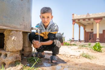 A young person washing their hands near their family’s home. 