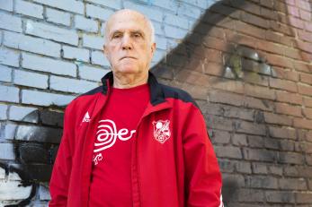 An 85 year old adult standing in front of a brick wall.