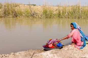 A person washing clothes in the same still pond where others bathe and draw drinking water in the wake of the floods.