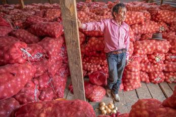 A farmer stands among bags of onions inside an onion storage facility that he opened with mercy corps help.