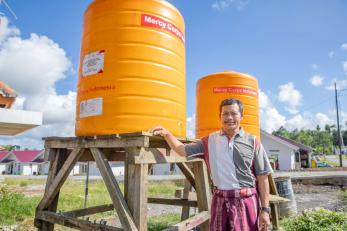A person standing in front of the mercy corps water tanks that were provided as part of the emergency response to the eruption of mount semeru.