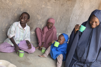 A mother and her children sitting outside drinking from green mugs