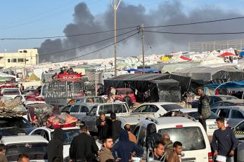 Displaced people heading from khan younis to rafah, after the israeli army ordered them to evacuate their homes in january 2024. explosions and smoke appear on the horizon as a result of israeli shelling.