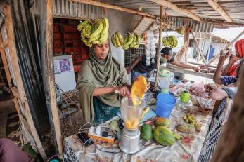A person scoops fresh fruit into a blender at their retail shop.