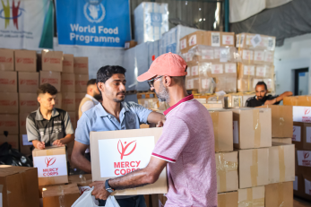 A person handing someone a box with the mercy corps logo on its side.