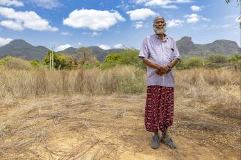 Kenyan man stands in rangeland with mountains in background.