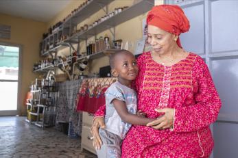 Senegalese female entrepreneur sits in her business smiling, with her grandson at her side..