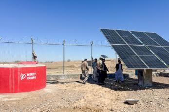 Afghan community members walking behind a solar panel array that powers the community water supply.