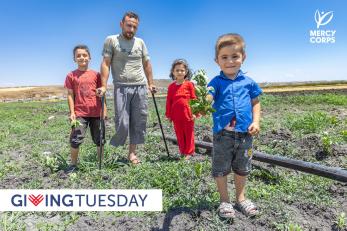 Syrian family standing in the middle of agricultural land, with young boy in foreground offering a bouquet to the camera.