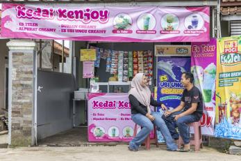Indonesian wife and husband sit in front of their beverage shop.
