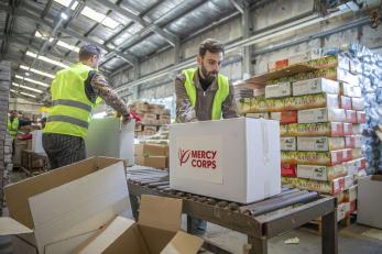 Mercy corps staff preparing boxes of emergency supplies in a warehouse.