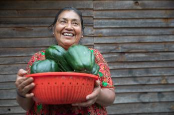 A smiling woman holds a bowl of peppers