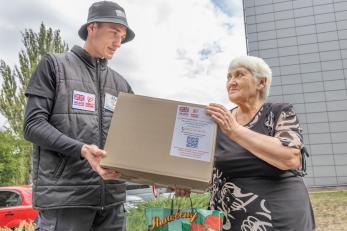 A man hands an aid box to a woman in ukraine