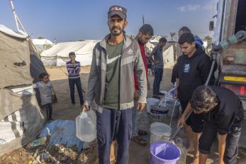 Man standing with other men collecting water and filling up water buckets.