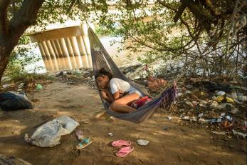 Joelbi lounges in the camp she shares with her mother, brother and 12 other youth who’ve bonded with them. she is pictured in a hammock beneath a tree.