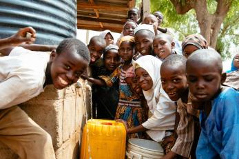 A group of children around a water tap, filling containers with fresh water