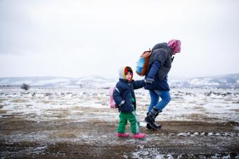 Woman and child walking in snow, wearing backpacks, holding hands