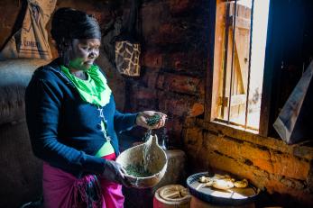 Kenyan woman pouring herbs from her hand into a wooden bowl