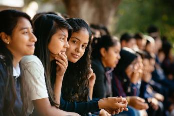 School children sitting in a row, one smiles at the camera.