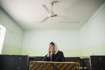 Iraqi woman with hands on face in a stark room.