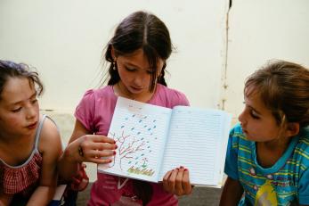 A young girl showing a drawing of a tree, flower, green grass and rain 