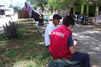 A mercy corps team member sits next to a man and looks at his phone in indonesia