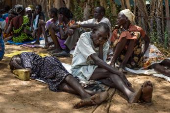 Two south sudanese wait in a group; one sleeps