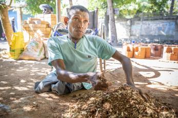 Freddie sitting on the ground working mud for a cookstove.