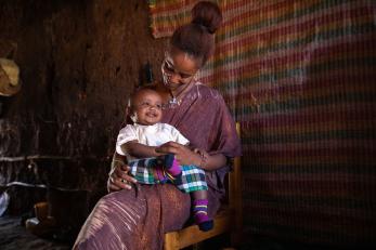 Rahima seated in a chair smiling down at her son, who she is holding on her lap