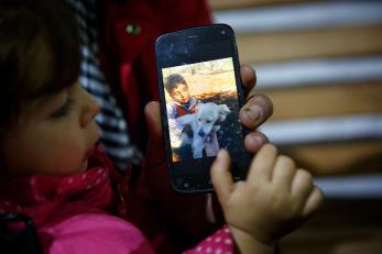 Young girl is looking at a photo of her brother in syria on her dad's phone.