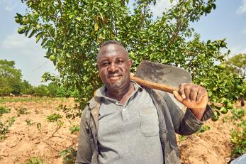 Nigerian man stands in field with a farm implement.