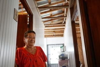 A woman wearing a red top stands in her reconstructed home in san juan, puerto rico.