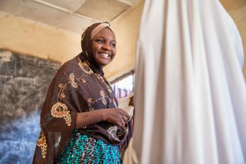 A smiling woman holds a pen and stack of paper in nigeria