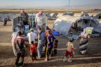 Women and children gathered around where plastic bins of supplies are being distributed