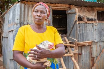 Kenyan woman holding a chicken outside a coop.